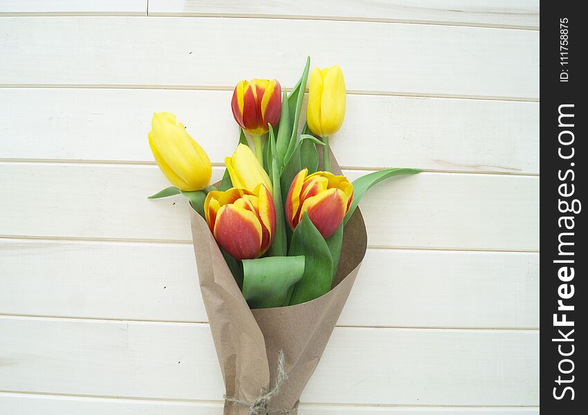 Spring bouquet for mom. View from above. The child gives a gift. A bouquet of yellow, red and orange tulips in a crafted package. Valentine`s Day. Wooden background. Mother`s Day and March 8th.
