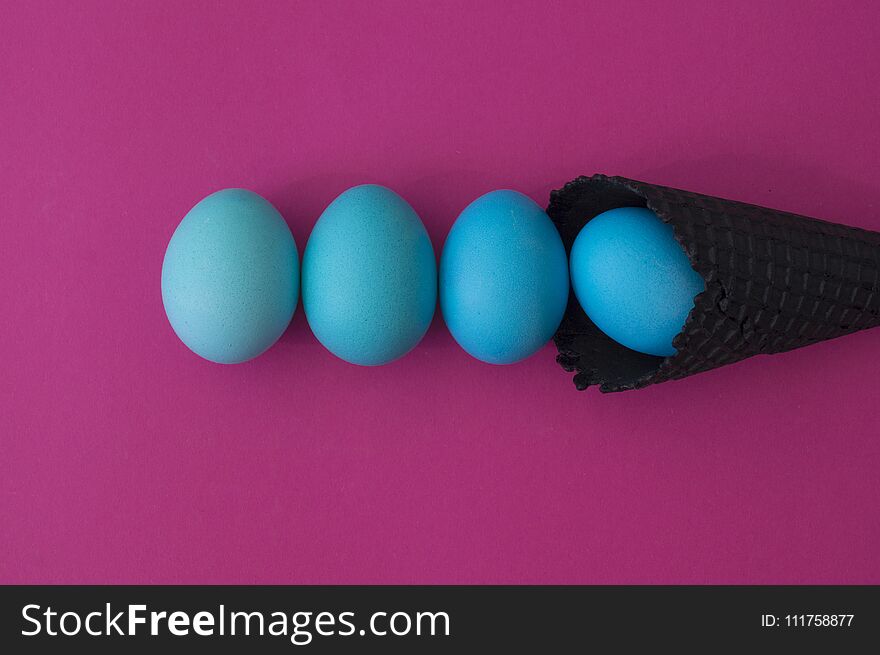 Easter. Blue eggs are poured from a waffle cone from ice cream. Black waffle cone. Ice cream egg. Pink background. Conceptual photo.