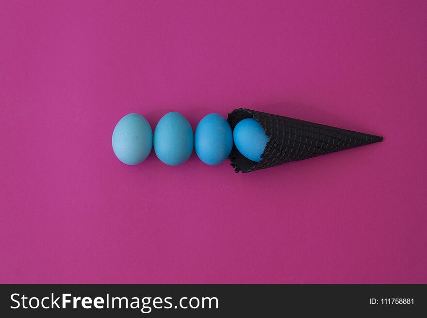 Easter. Blue eggs are poured from a waffle cone from ice cream. Black waffle cone. Ice cream egg. Pink background. Conceptual photo.