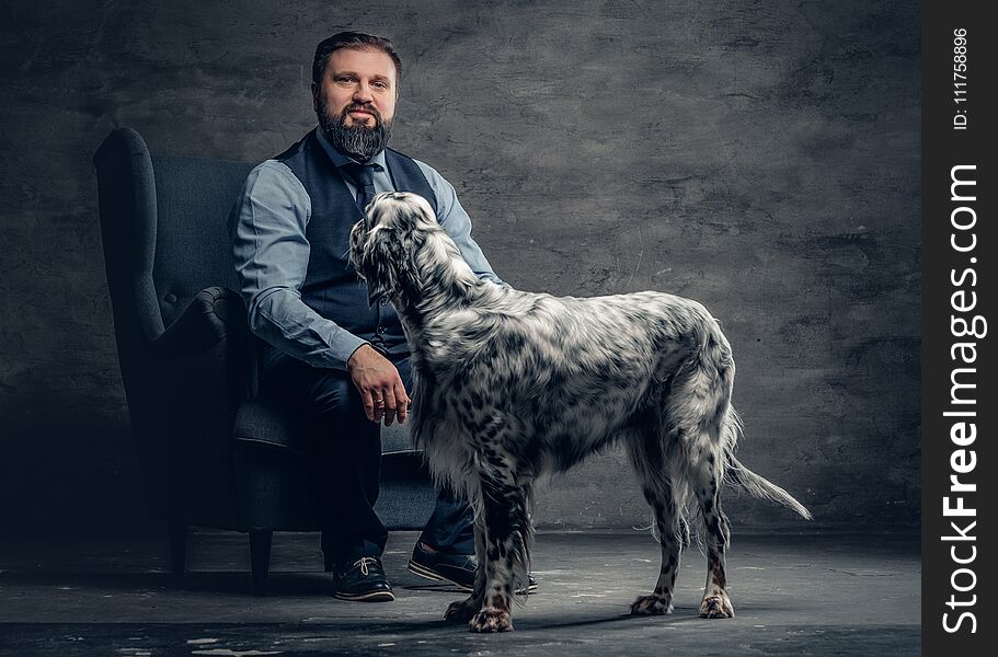 Stylish bearded male sits on a chair and the Irish setter dog.