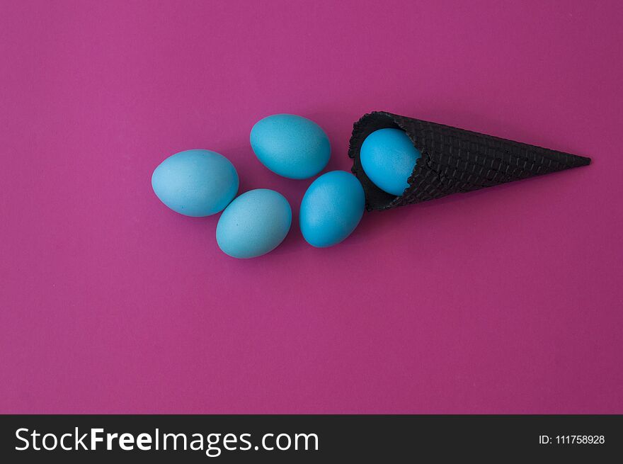 Easter. Blue eggs are poured from a waffle cone from ice cream. Black waffle cone. Ice cream egg. Pink background. Conceptual photo.