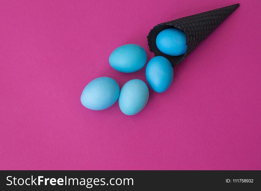 Easter. Blue eggs are poured from a waffle cone from ice cream. Black waffle cone. Ice cream egg. Pink background. Conceptual photo.