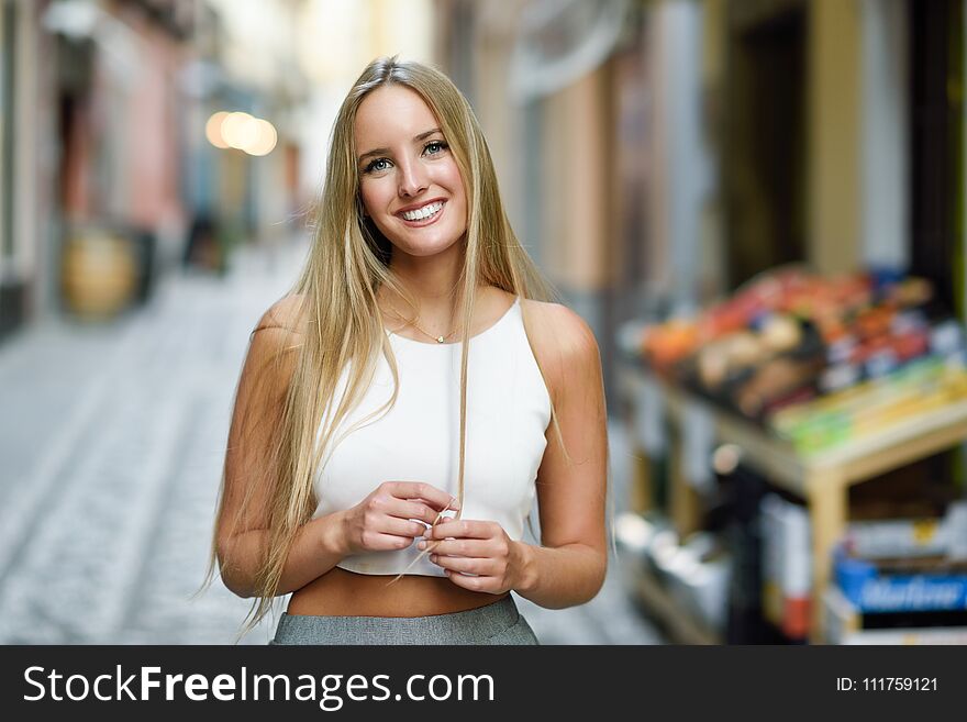 Smiling young woman in urban background. Blond girl wearing with nice hair casual clothes in the street. Straight hairstyle. Smiling young woman in urban background. Blond girl wearing with nice hair casual clothes in the street. Straight hairstyle.