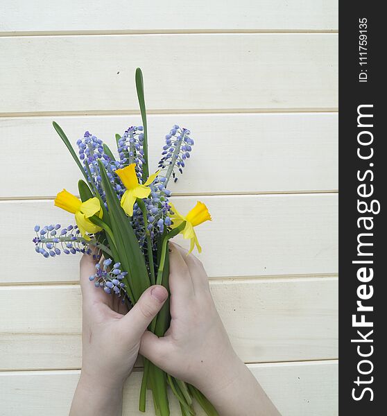 Children`s hands collect a bouquet as a gift. A gift for mom. Spring festive bouquet in a crafting package. Pruning flowers. The child is a florist. Wooden background. Field bouquet. Eco-style.