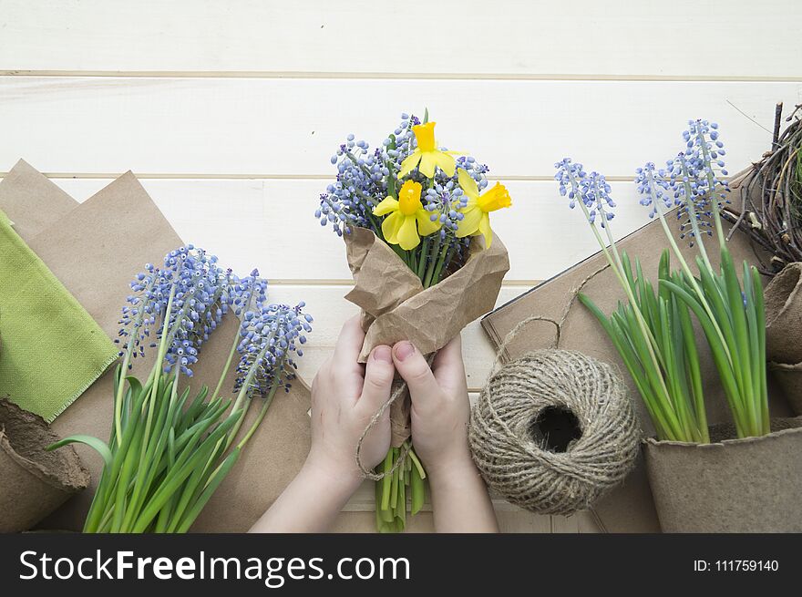 Children`s hands collect a bouquet as a gift. A gift for mom. Spring festive bouquet in a crafting package. Pruning flowers. The child is a florist. Wooden background. Field bouquet. Eco-style.