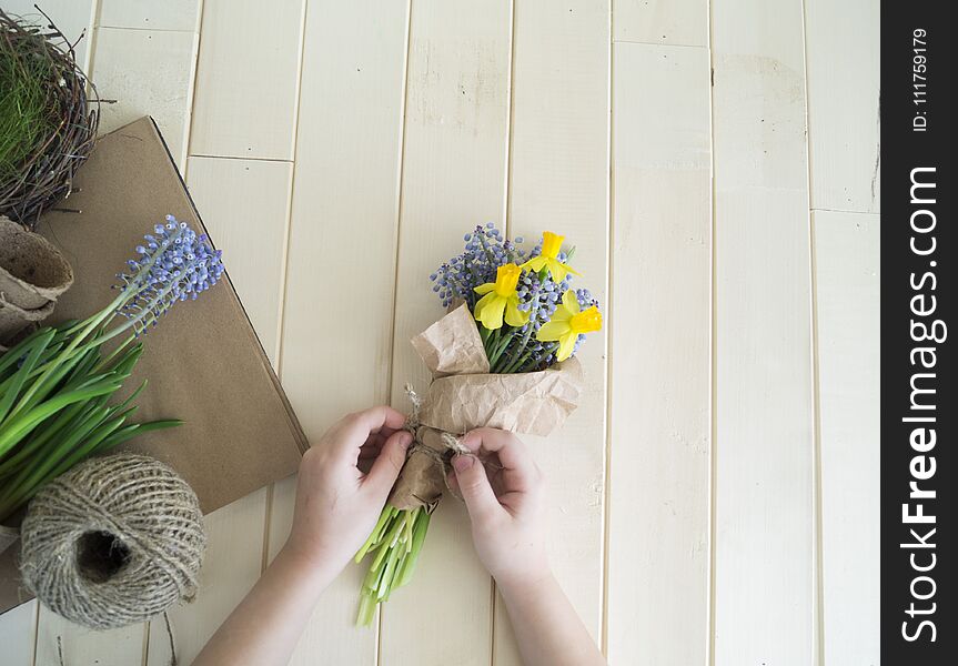 Children`s hands collect a bouquet as a gift. A gift for mom. Spring festive bouquet in a crafting package. Pruning flowers. The child is a florist. Wooden background. Field bouquet. Eco-style.
