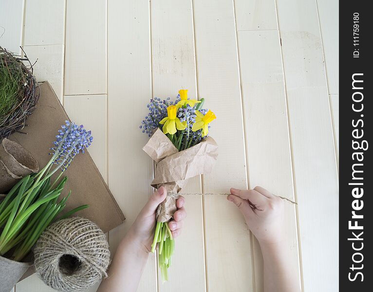 Children`s hands collect a bouquet as a gift. A gift for mom. Spring festive bouquet in a crafting package. Pruning flowers. The child is a florist. Wooden background. Field bouquet. Eco-style.