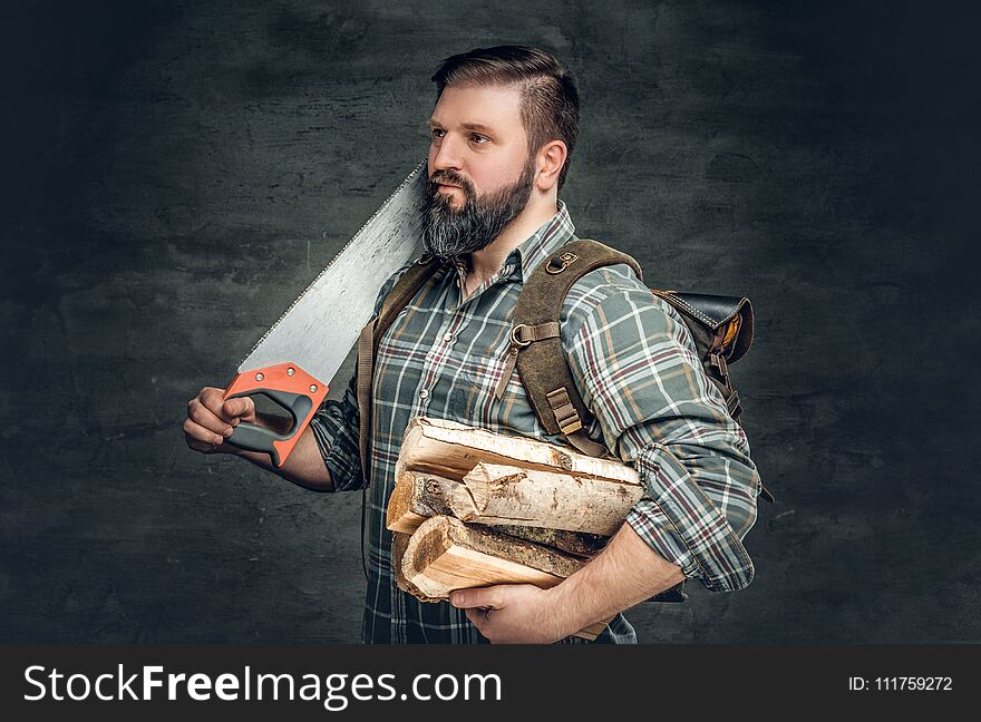 Bearded male holds fire woods and hand saw. Bearded male holds fire woods and hand saw.