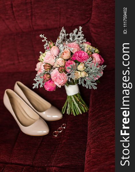 Wedding bouquet with purple and pink roses. Wedding accessories are lying on a red armchair. Wedding