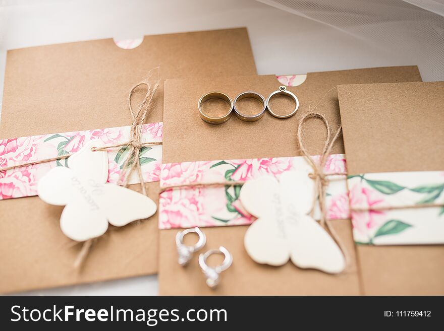 Two golden rings and engagement ring lying on the wedding invitations in the craft envelopes. Wedding concept. Wedding accessories.