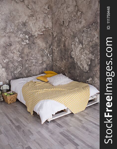 A loft style bedroom with recycled pallet bed. White and yellow bedding on bed with bedhead in loft bedroom interior