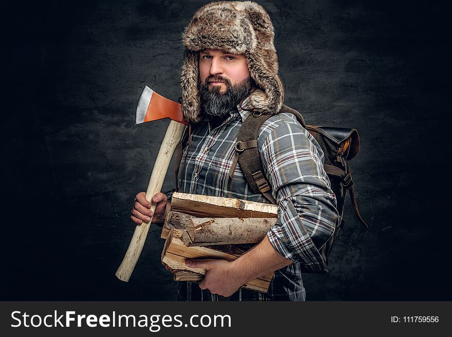 Portrait of brutal bearded hunter male dressed in a fleece shirt and a hat from a fur holds an axe on his shoulder. Portrait of brutal bearded hunter male dressed in a fleece shirt and a hat from a fur holds an axe on his shoulder.