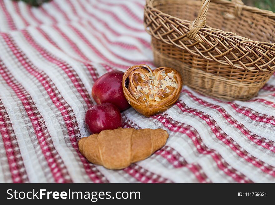 Romantic picnic in the garden - a basket with bakery and apples. Picnic on the lawn. Objects for picnic on a coverlet. .