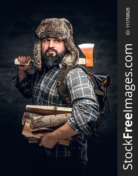 Portrait of brutal bearded hunter male dressed in a fleece shirt and a hat from a fur holds an axe on his shoulder. Portrait of brutal bearded hunter male dressed in a fleece shirt and a hat from a fur holds an axe on his shoulder.