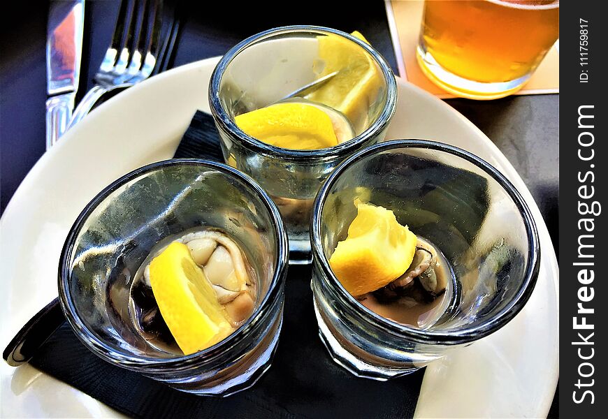 Three Oyster Shooters with Lemon in shot glasses, o a white plate, with a glass of beer