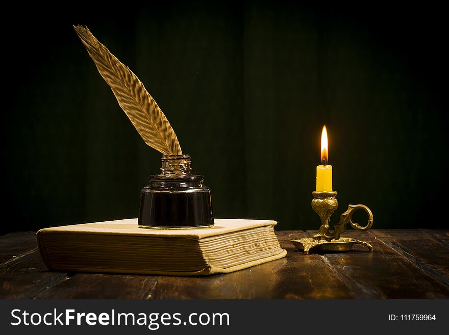 Education and writing concept, pen in ink bottle and candlestick with candle on wooden table on dark background. Education and writing concept, pen in ink bottle and candlestick with candle on wooden table on dark background.