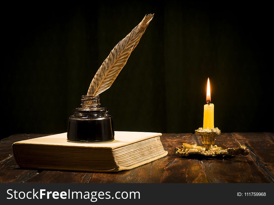 Education and writing concept, pen in ink bottle and candlestick with candle on wooden table on dark background. Education and writing concept, pen in ink bottle and candlestick with candle on wooden table on dark background.