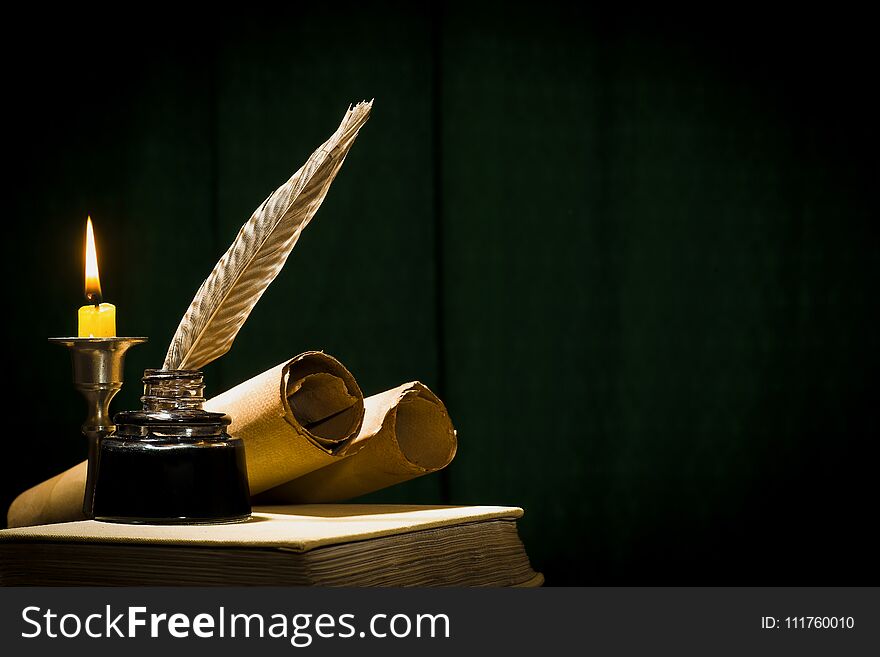 The concept of education and writing, a pen in an inkwell and a candle with a candle, and a book on a dark background.