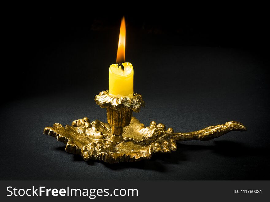 Vintage candlestick with a lit candle on a black background