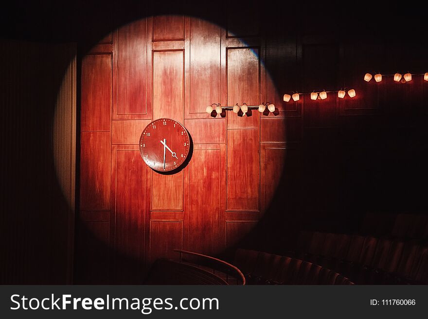 Wooden watch on a wood panel covered wall lit by a stage light showing half past four