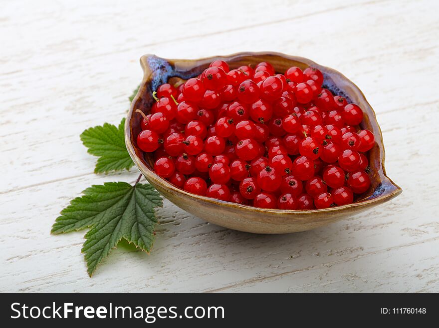 Red currants with leaves in the bowl on wood