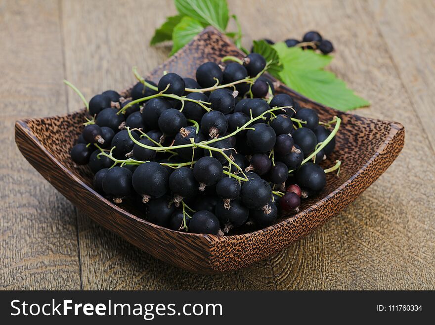 Black currants heap with leaves on wood background