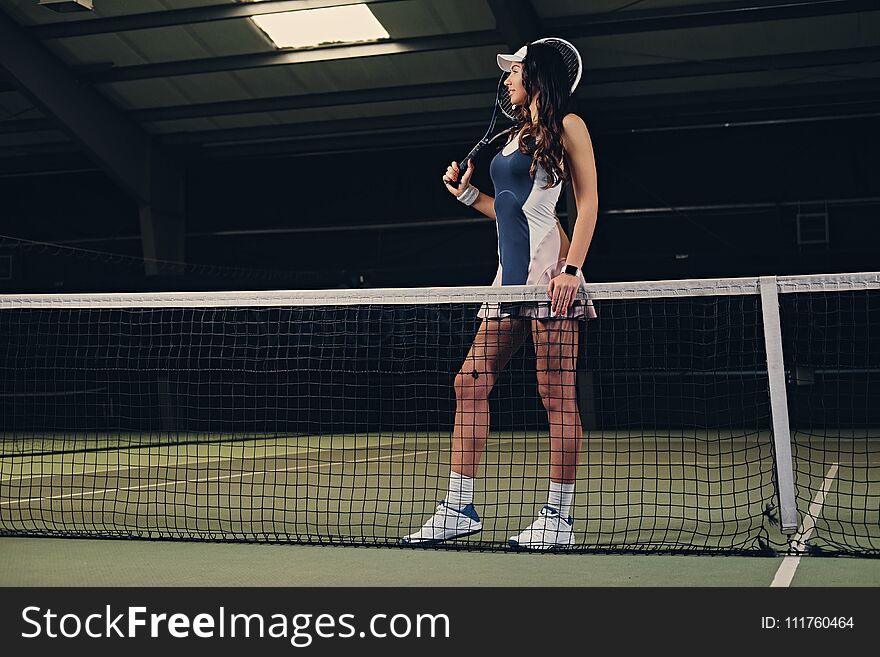 brunette female tennis player posing on an indoor tennis court.