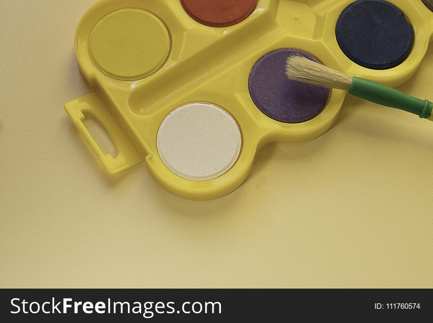 Watercolors in bright yellow box with big brush for kids are on the table . Kids art concept. Watercolors in bright yellow box with big brush for kids are on the table . Kids art concept.