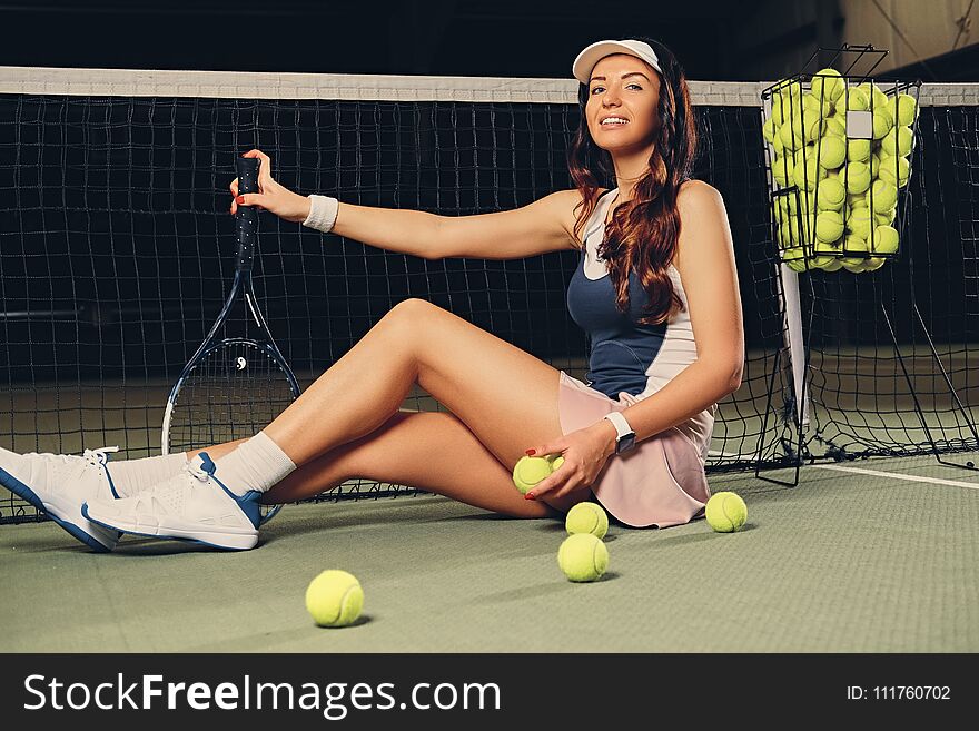 Female tennis player sits in a court and holds playing rocket.