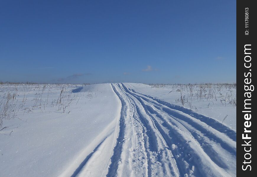 Road to horizon in the field in the wintertime. Deep snowmarks on the snowdrifts. Sunny conditions, clear sky, without clouds. Road to horizon in the field in the wintertime. Deep snowmarks on the snowdrifts. Sunny conditions, clear sky, without clouds.