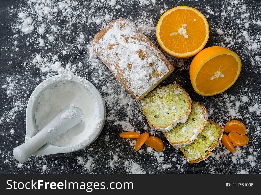 Mint cake sprinkled with powdered sugar on dark surface with fresh oranges mandarins.