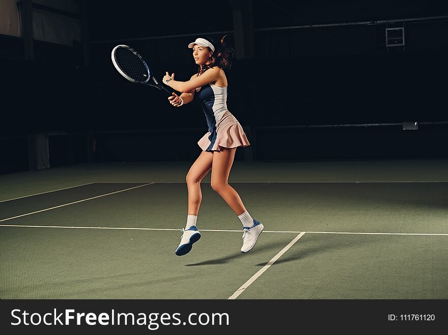 Full body portrait of female tennis player in action in a tennis court indoor.