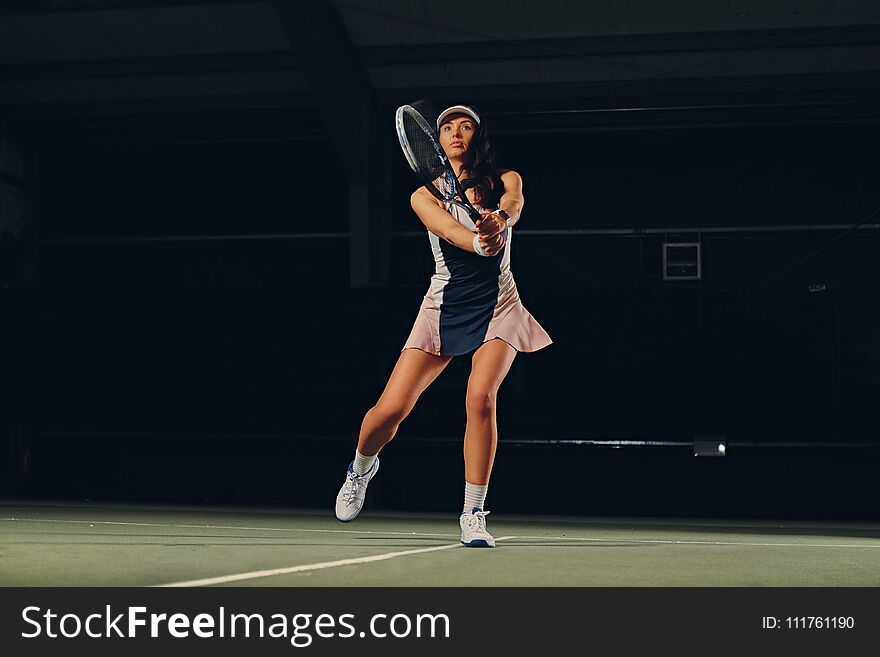 Full body portrait of female tennis player in a jump on a tennis court over dark background. Full body portrait of female tennis player in a jump on a tennis court over dark background.