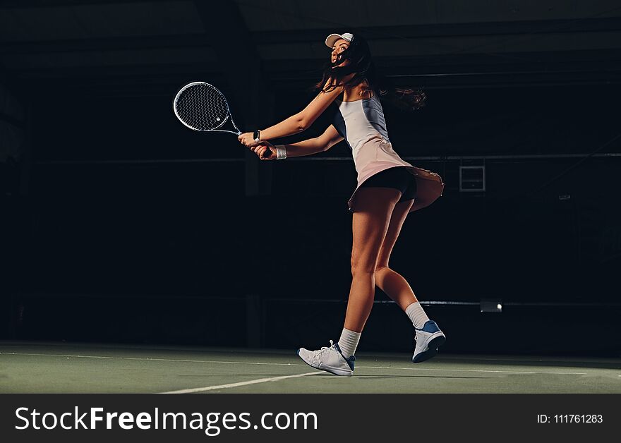 Full body portrait of female tennis player in action in a tennis court indoor.