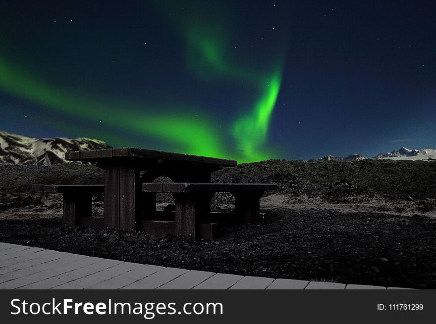 Picture of phenomenal green Aurora borealis in Iceland sky with a bench in the foreground
