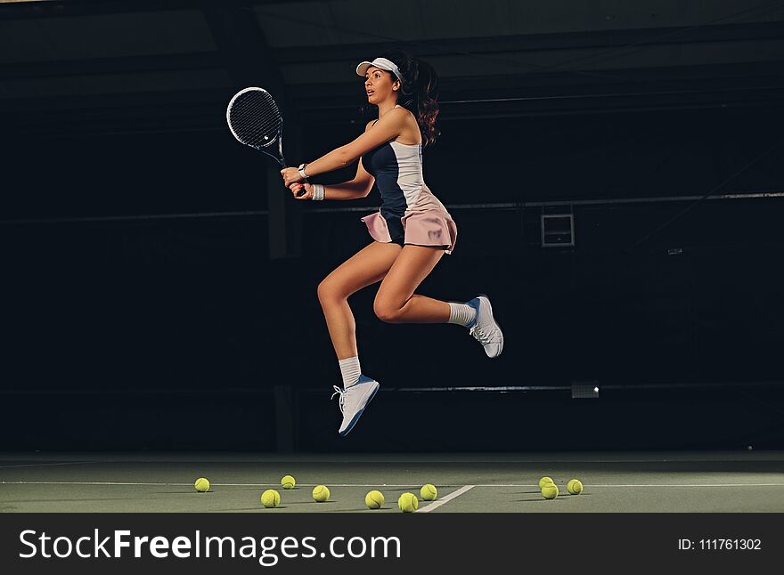 Full body portrait of female tennis player in a jump on a tennis court over dark background. Full body portrait of female tennis player in a jump on a tennis court over dark background.