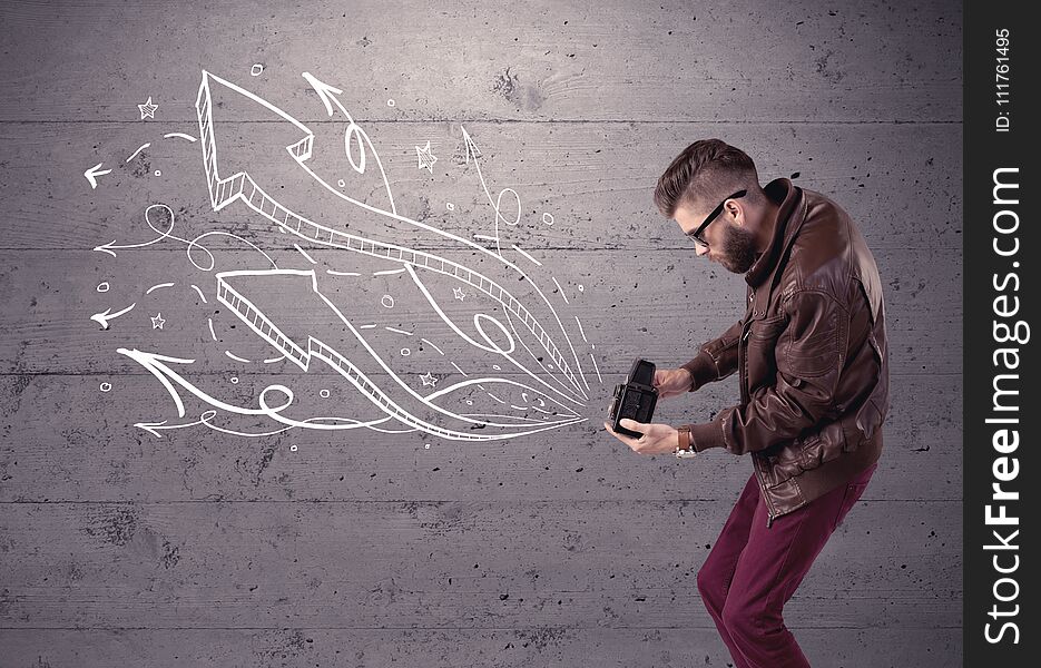 A hipster guy opening his point of view through looking a vintage camera concept with illustratied drawn arrows on urban wall. A hipster guy opening his point of view through looking a vintage camera concept with illustratied drawn arrows on urban wall
