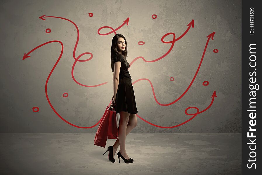 An elegant young lady in black holding red shopping bags in front of urban wall background with drawn red arrows and circles concept. An elegant young lady in black holding red shopping bags in front of urban wall background with drawn red arrows and circles concept