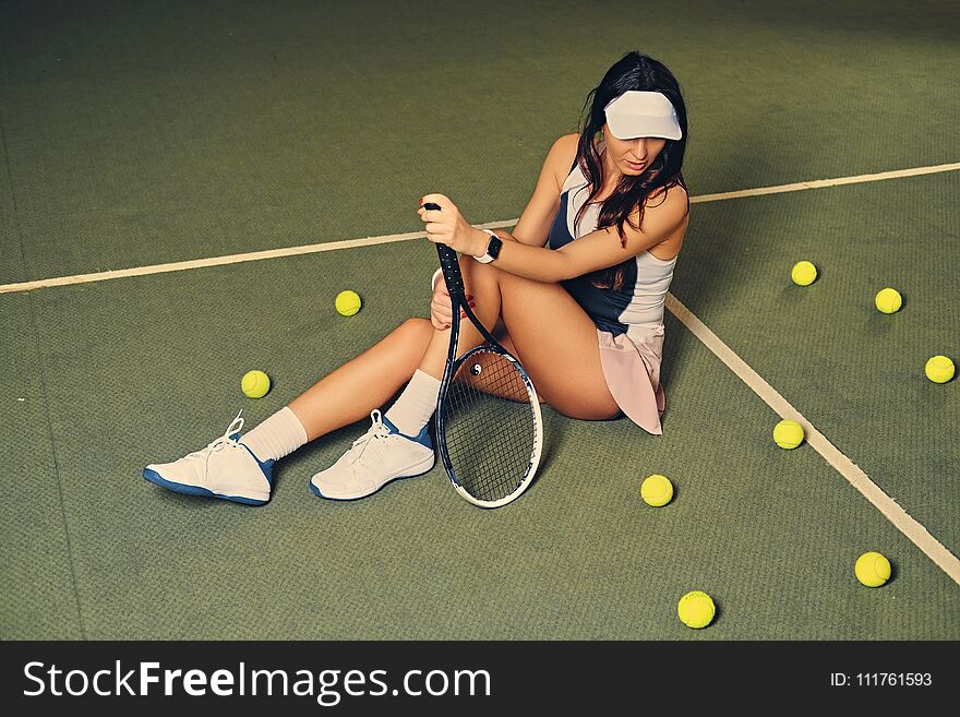 Female tennis player sits in a court and holds playing rocket.