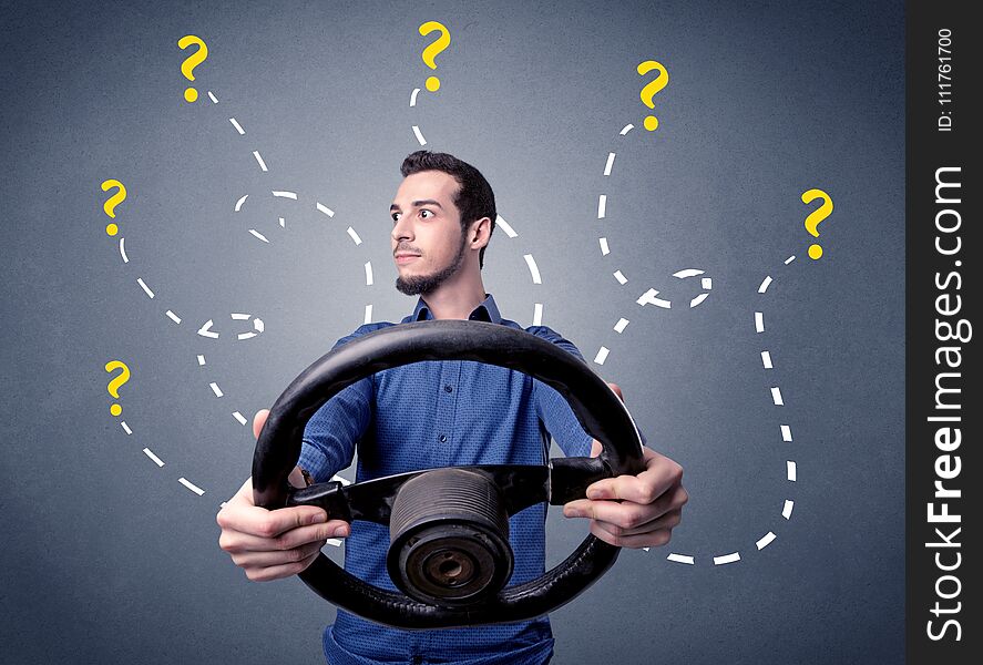 Young man holding black steering wheel with question marks around him. Young man holding black steering wheel with question marks around him