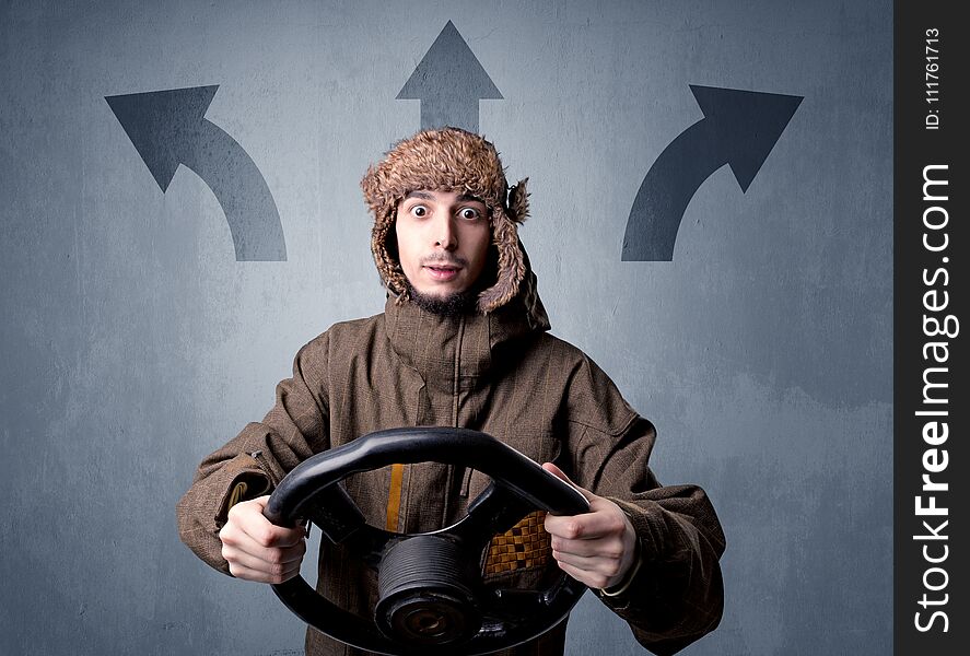 Young man holding black steering wheel with three arrows above his head pointing in different directions. Young man holding black steering wheel with three arrows above his head pointing in different directions