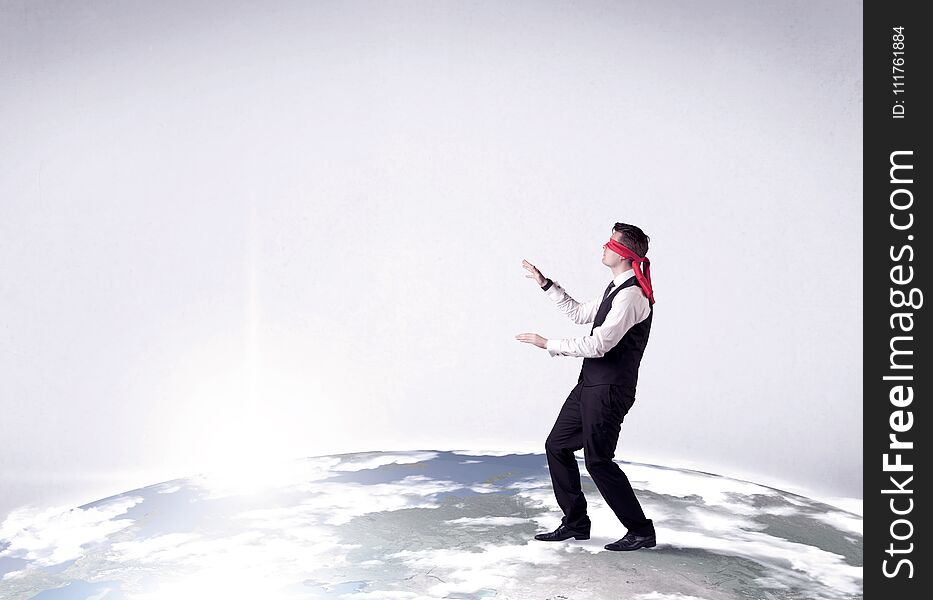 Young blindfolded businessman steps on a realistic globe. Young blindfolded businessman steps on a realistic globe