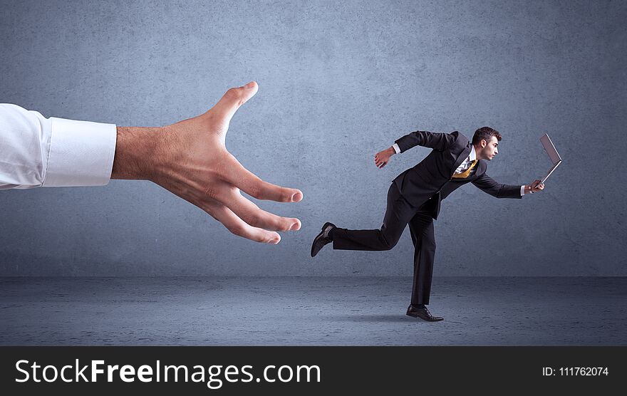 Young miniature businessman running from a big hand with blueish grey background. Young miniature businessman running from a big hand with blueish grey background