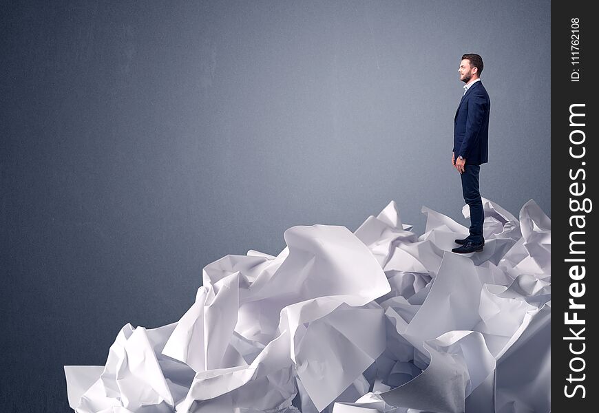 Thoughtful young businessman standing on a pile of crumpled paper with a light grey background. Thoughtful young businessman standing on a pile of crumpled paper with a light grey background