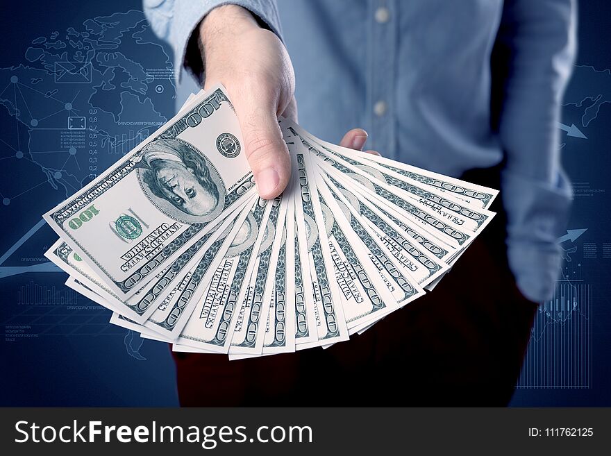 Young businessman holding large amount of bills with blue charts in the background. Young businessman holding large amount of bills with blue charts in the background