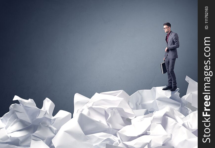 Thoughtful young businessman standing on a pile of crumpled paper with a blueish grey background. Thoughtful young businessman standing on a pile of crumpled paper with a blueish grey background