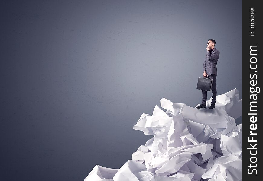 Thoughtful young businessman standing on a pile of crumpled paper with a dark grey background. Thoughtful young businessman standing on a pile of crumpled paper with a dark grey background