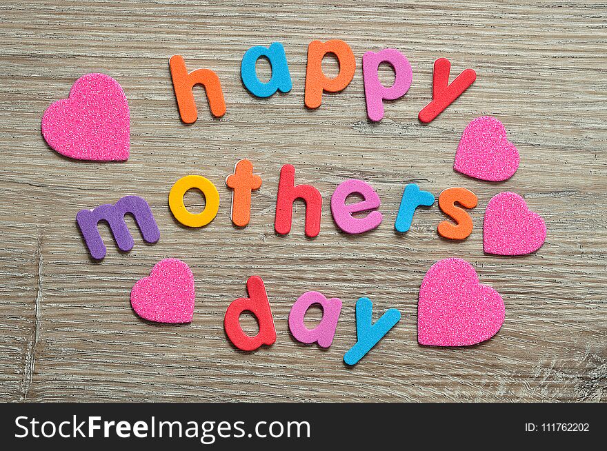 Happy mothers day in colorful letters on a wooden background with pink hearts. Happy mothers day in colorful letters on a wooden background with pink hearts