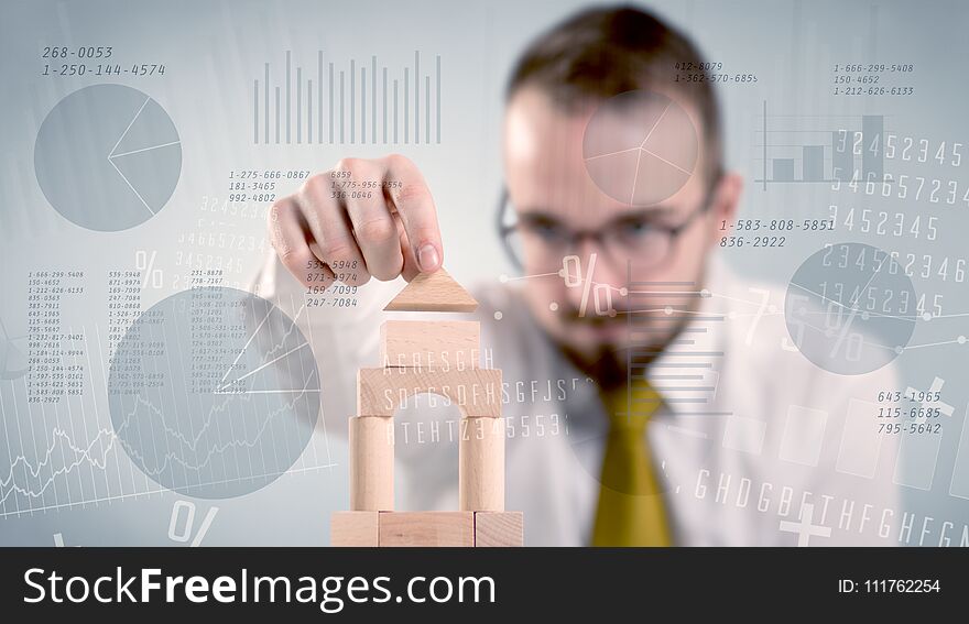 Young handsome businessman using wooden building blocks with data and numbers around him. Young handsome businessman using wooden building blocks with data and numbers around him