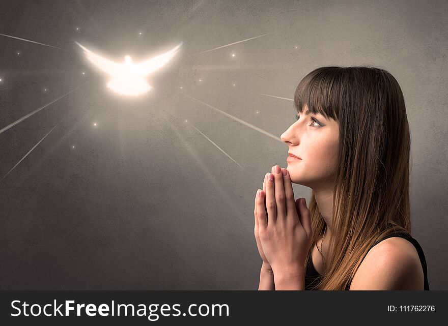 Young woman praying on a grey background with a sparkling bird above her. Young woman praying on a grey background with a sparkling bird above her